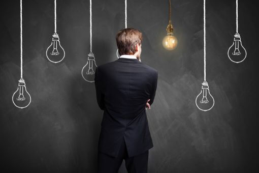 壁に書かれた電球の絵を見ながら何かを考える男性